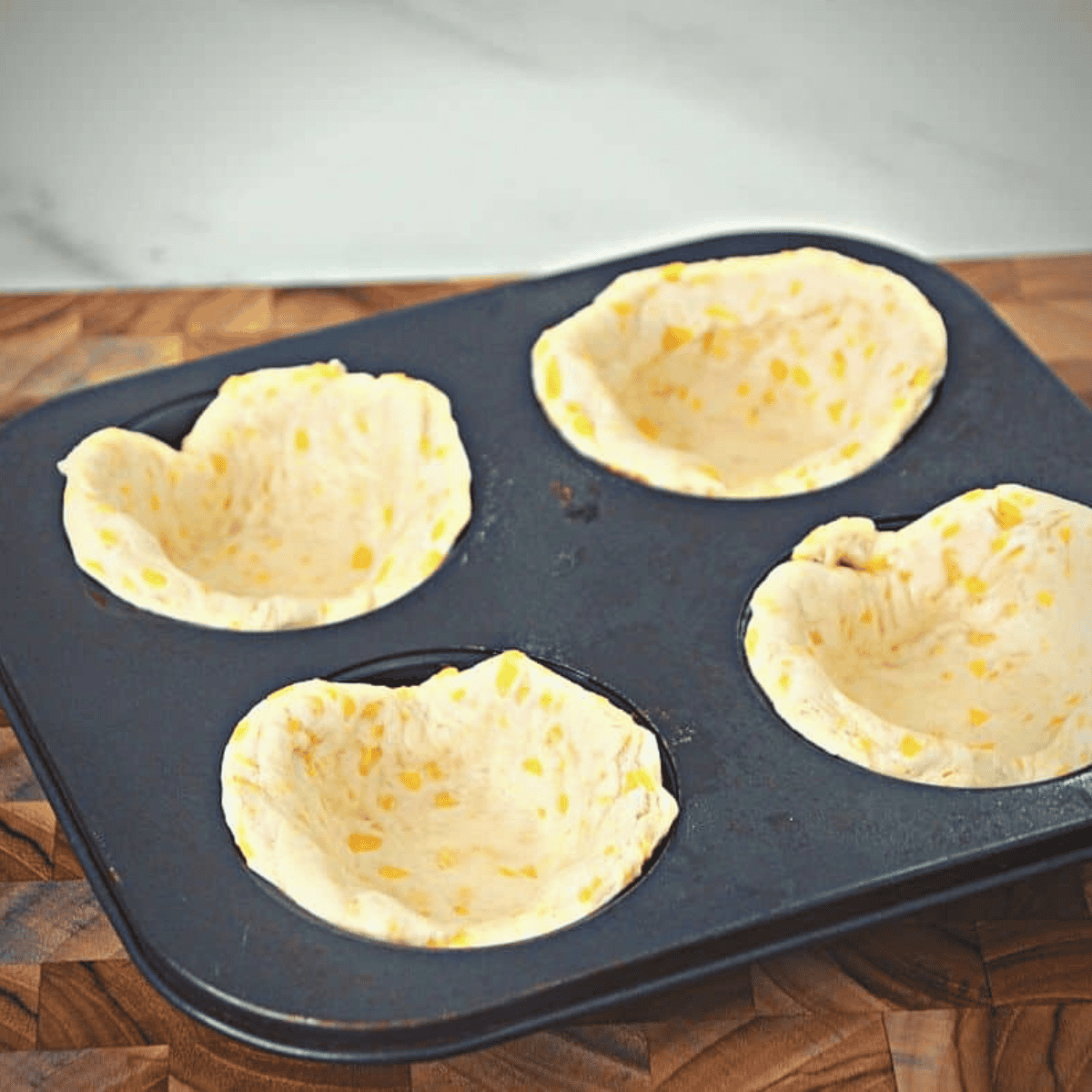 Pressing biscuit dough into a sprayed muffin tin to create small cups for air frying.