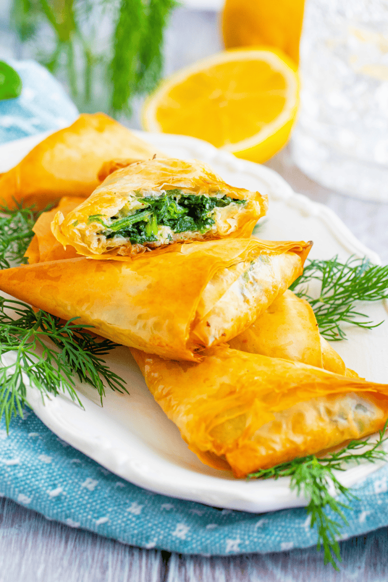 Golden air fryer spanakopita triangles filled with spinach, feta, and ricotta on a serving plate.