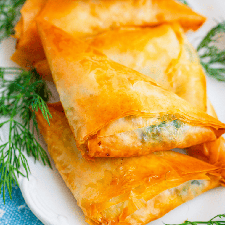 Golden air fryer spanakopita cups filled with spinach, feta, and herbs on a serving plate.