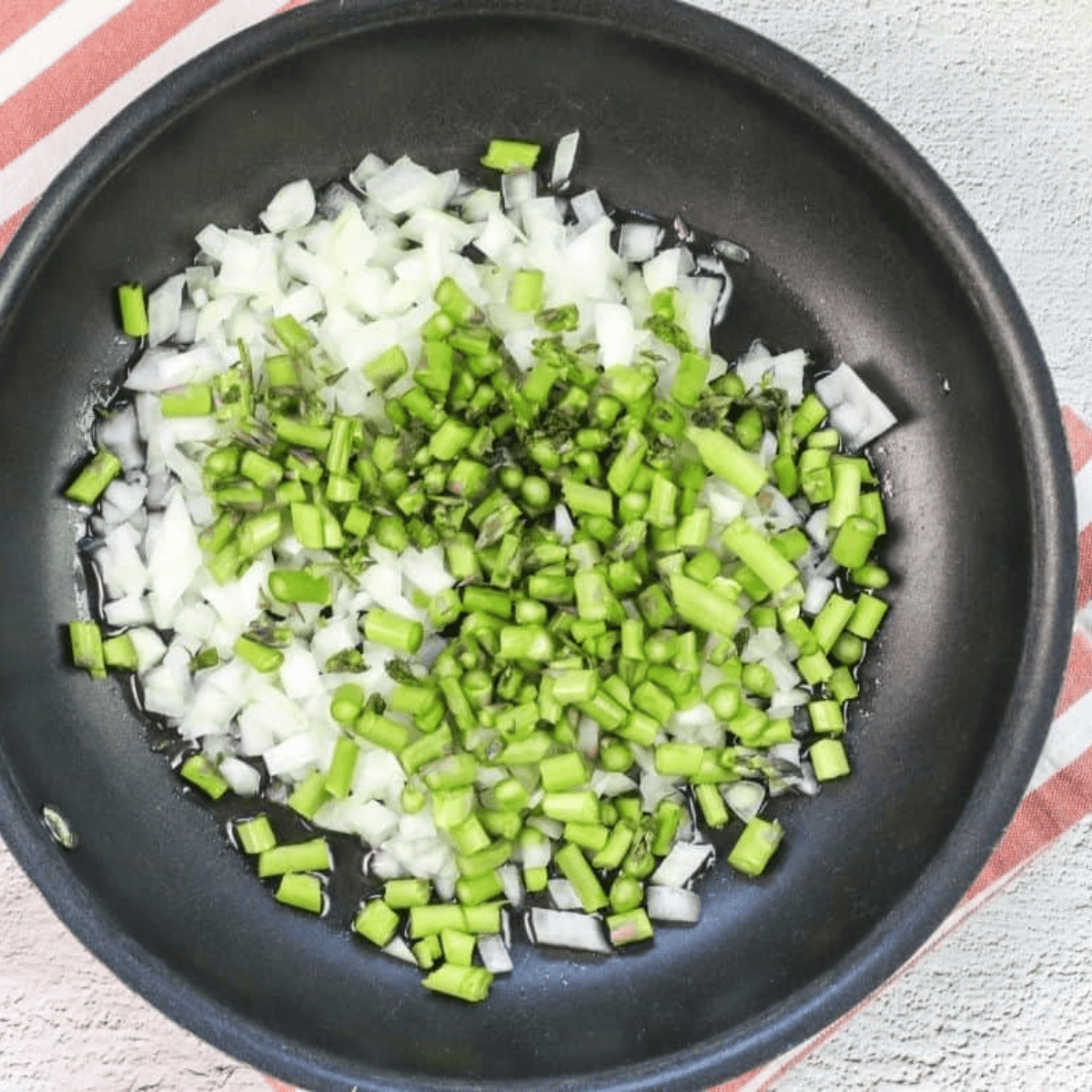 Sautéing yellow onion and asparagus in a 10-inch skillet with olive oil until tender