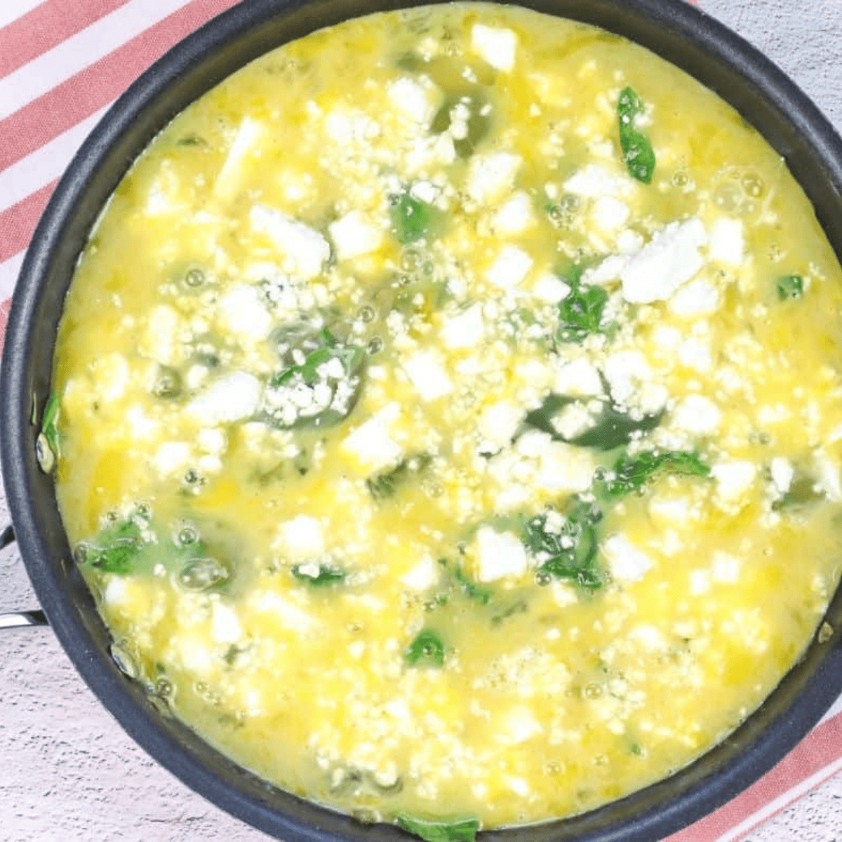 Pour egg mixture over sautéed vegetables in skillet, top with cheddar and feta cheeses, cooking until edges start to set