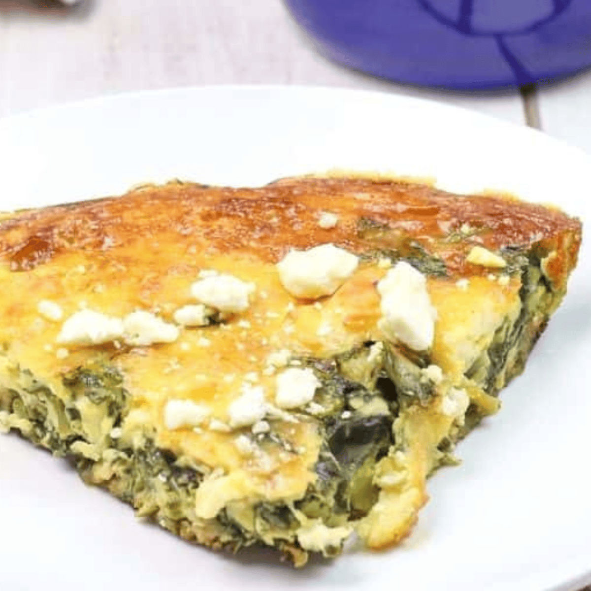 Air fryer asparagus, spinach, and cheese frittata cooked golden brown in a skillet, topped with melted cheddar and crumbled feta cheese, ready to serve for breakfast or brunch.