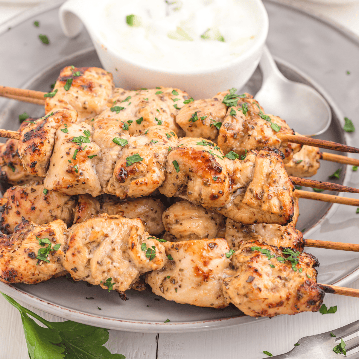 Air Fryer Greek Chicken Kebabs on a white plate with a side of creamy tzatziki sauce