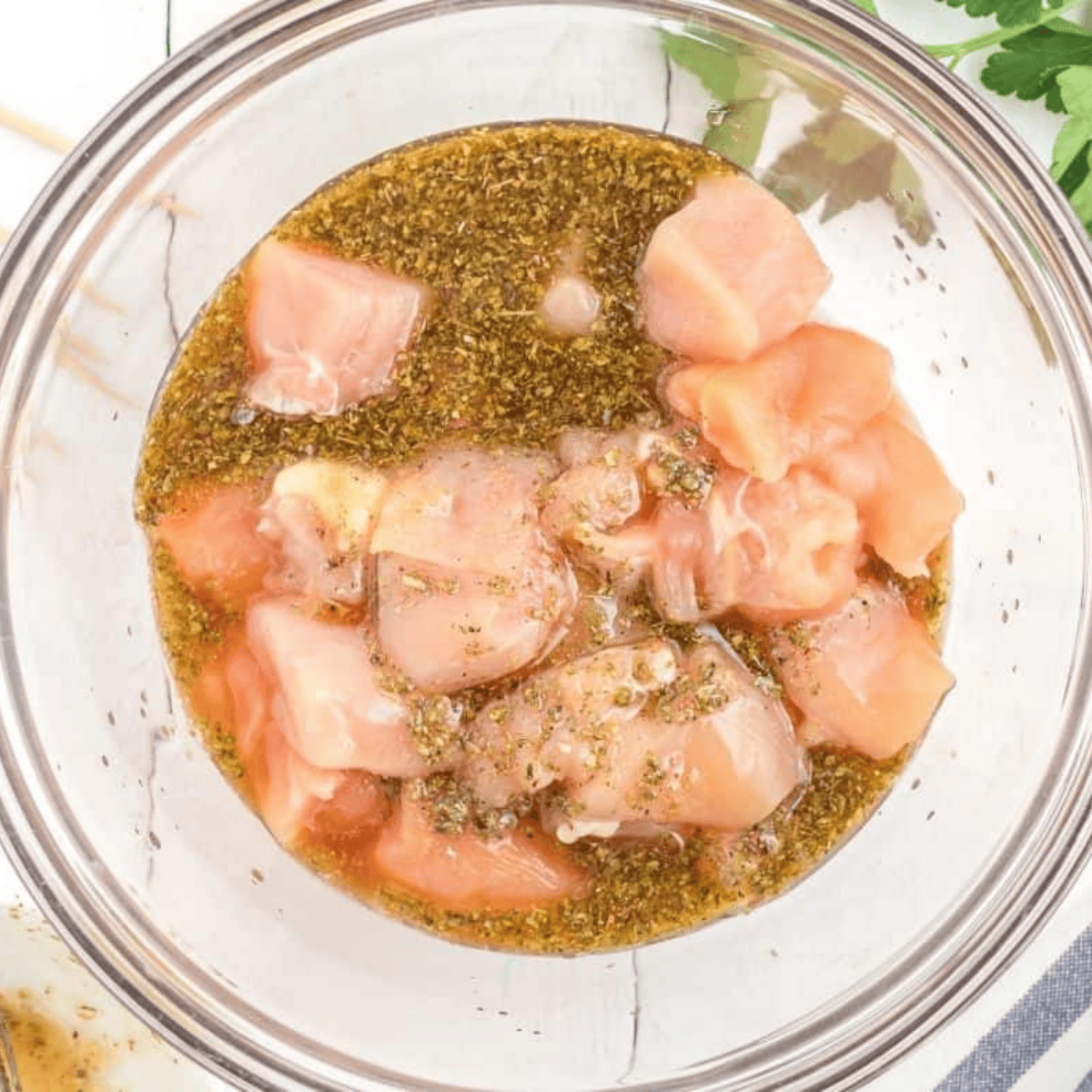 Cubed chicken breast tossed in Greek marinade in a bowl for Air Fryer Greek Chicken Kebabs