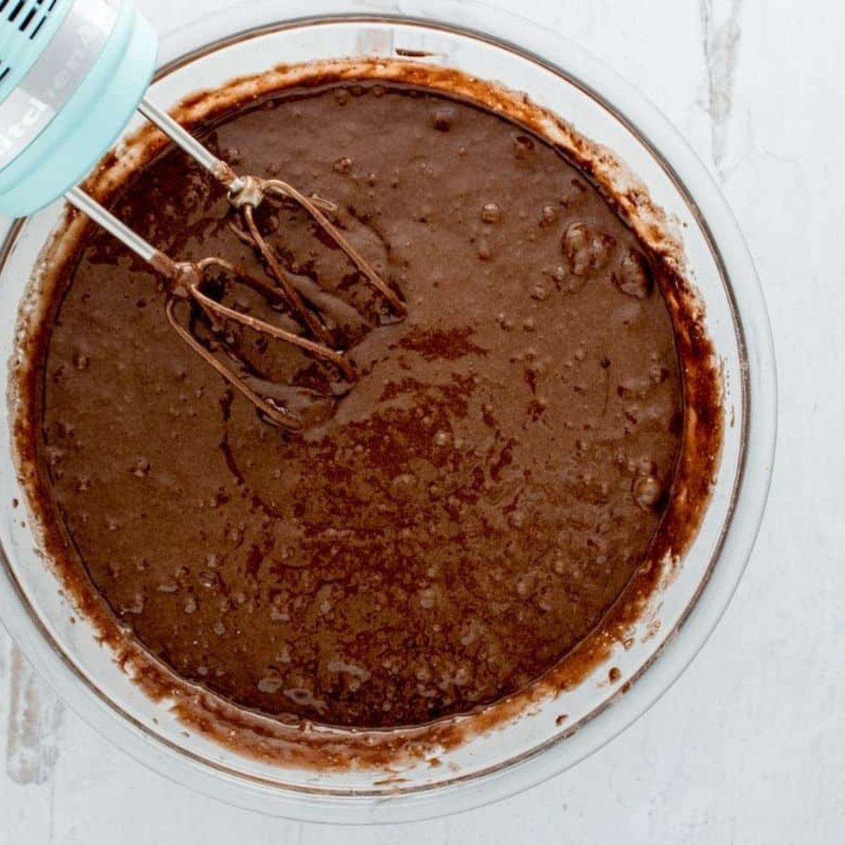 Mixing chocolate cake ingredients in a bowl before pouring into greased cake pans