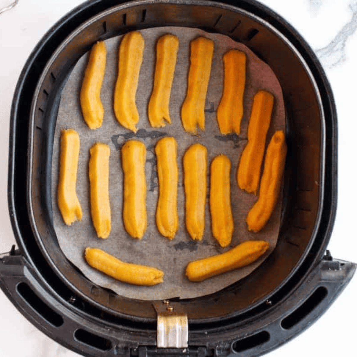 Piping pumpkin churro dough into an air fryer basket lined with parchment