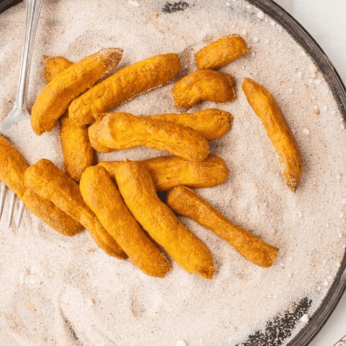 Freshly air-fried pumpkin churros being rolled in cinnamon sugar