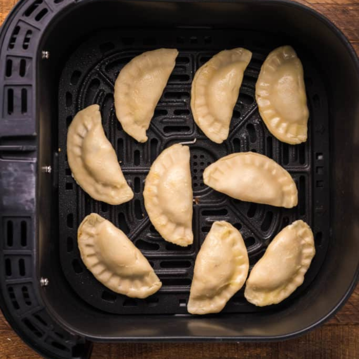 Empanadas brushed with melted butter in a single layer in an air fryer basket