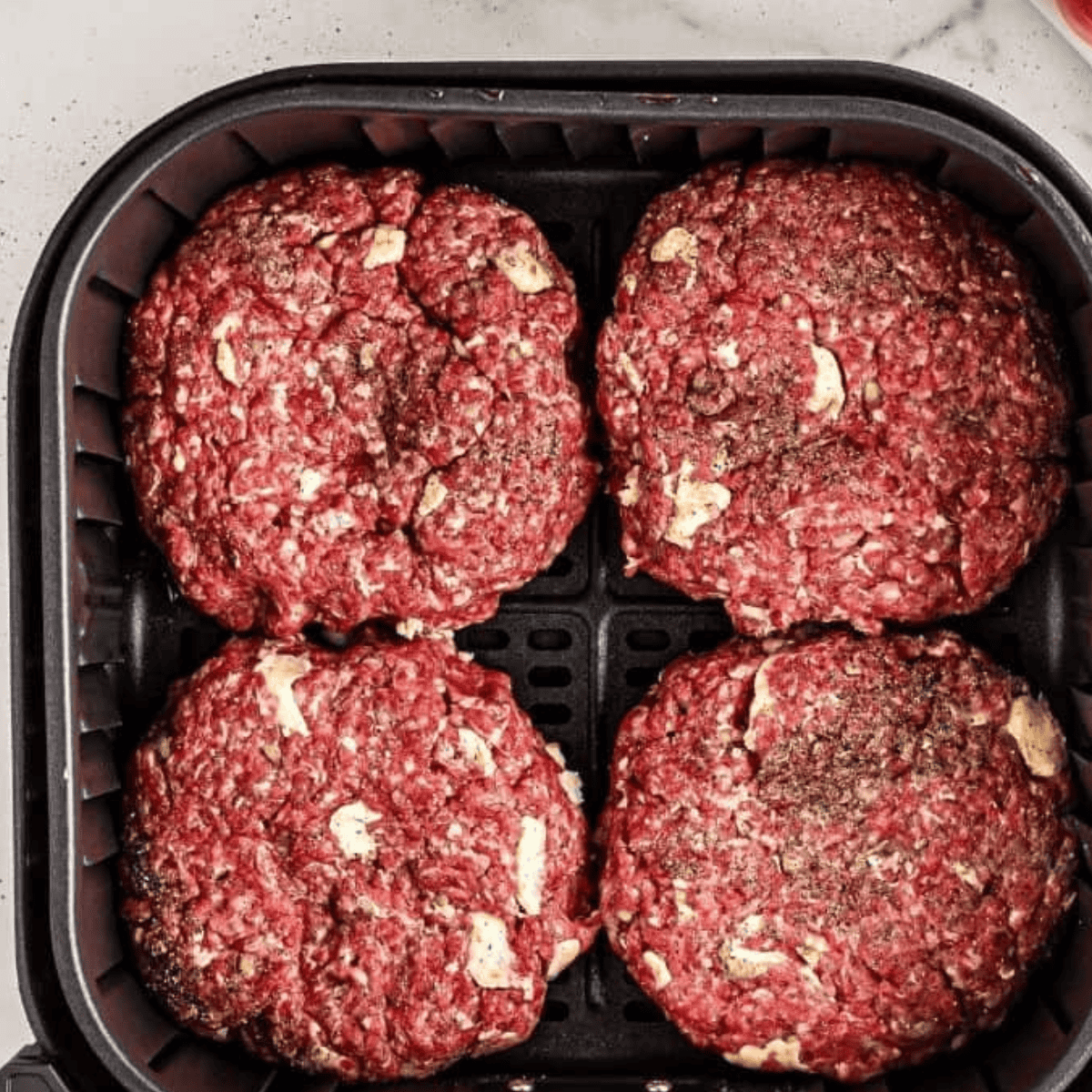 Top view of four raw patties in an air fryer.