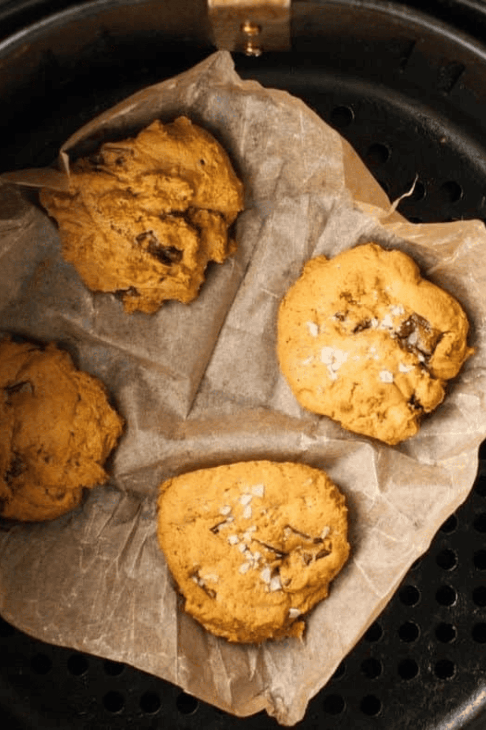 Pumpkin cookie dough scooped and flattened on parchment-lined air fryer basket, ready to bake.