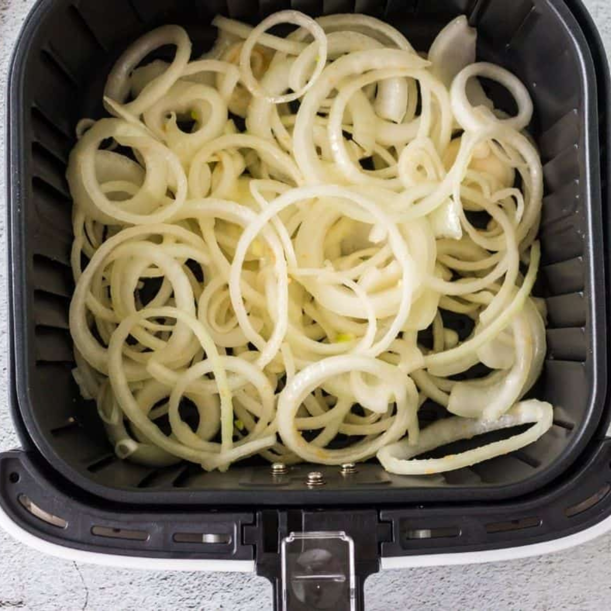 Sliced onions tossed with olive oil, salt, and butter pieces in a foil pan