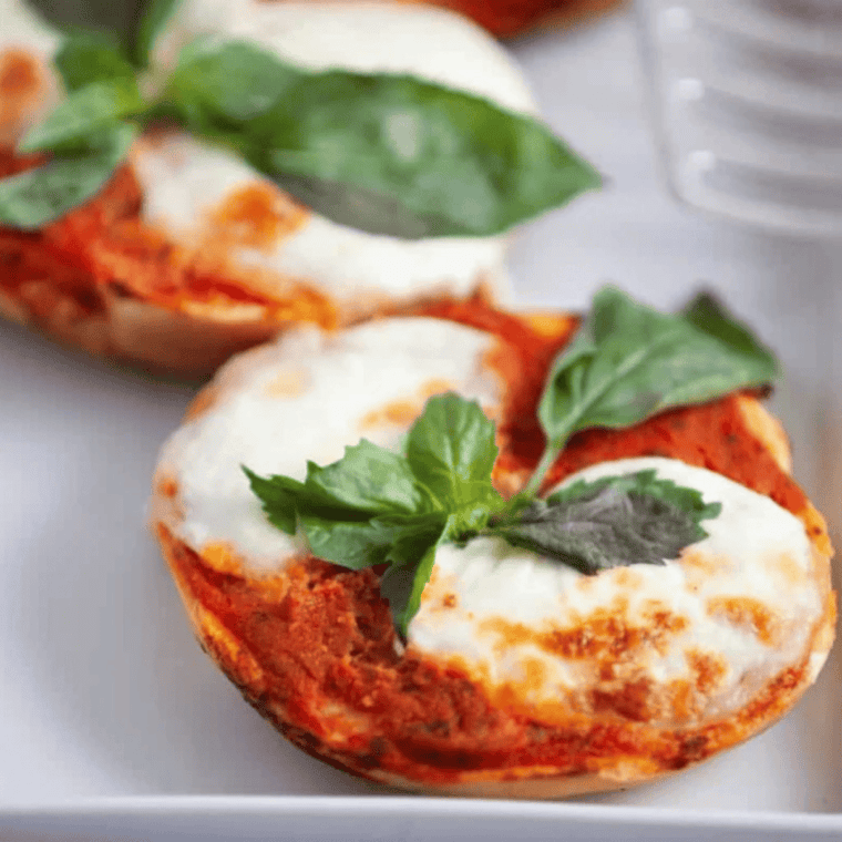 Air fryer Margherita pizza bagels topped with fresh mozzarella, tomato slices, and basil leaves.