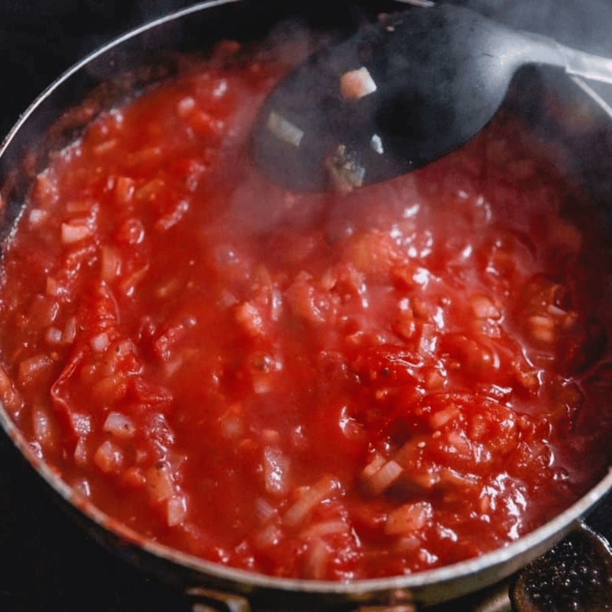 Homemade marinara sauce simmering in a pan with onion, garlic, and tomatoes