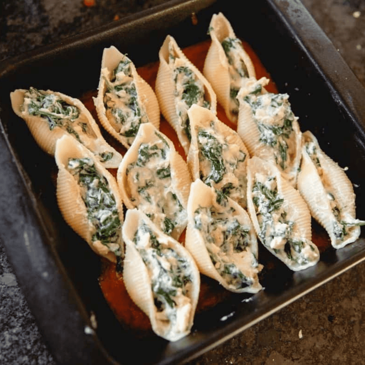 Stuffed spinach pasta shells arranged over marinara in an air fryer pan, topped with mozzarella