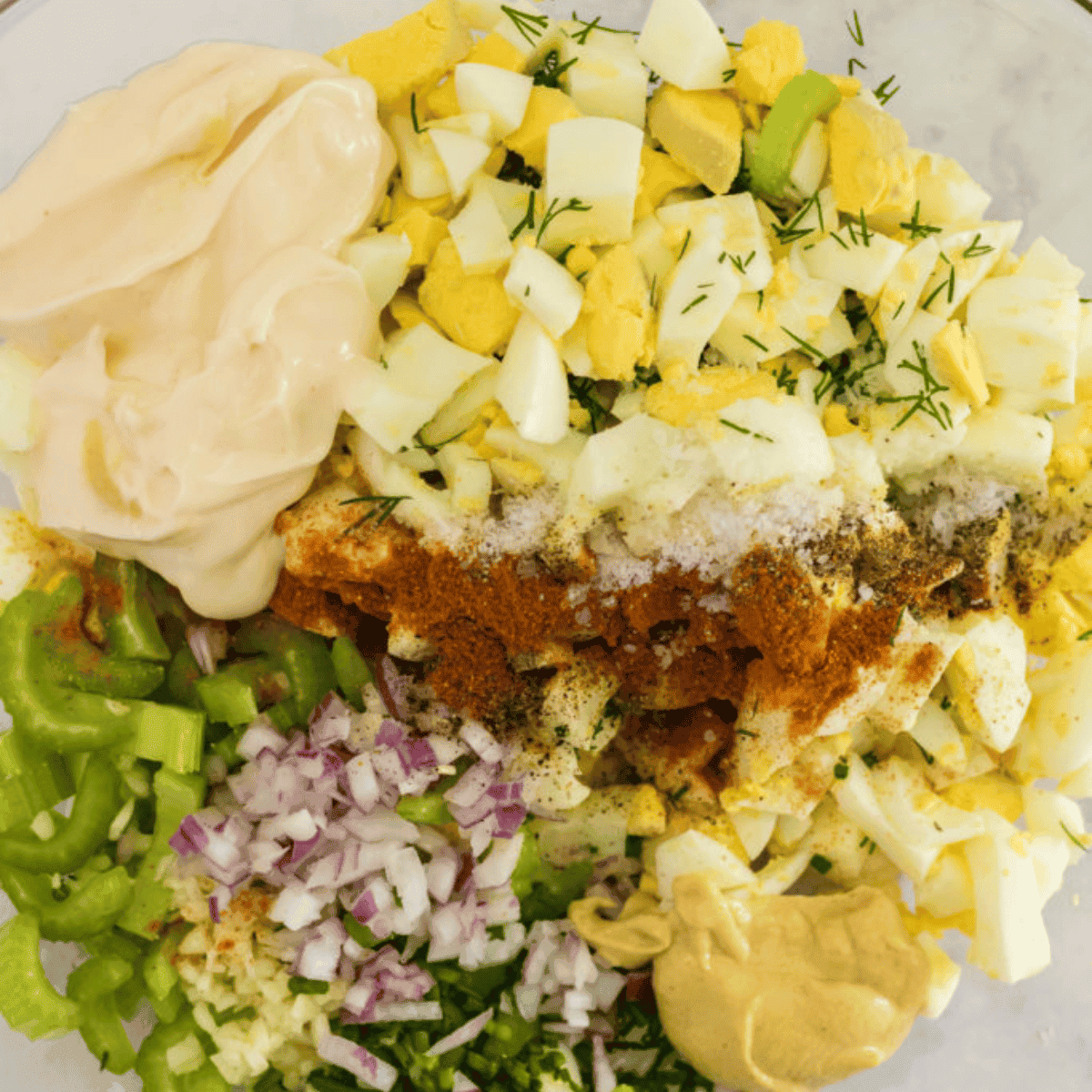 Creamy dressing mixed in a small bowl, then poured over chopped eggs, pickles, celery, and onions in a large mixing bowl, stirred together and ready to serve on toast, croissants, or lettuce wraps.