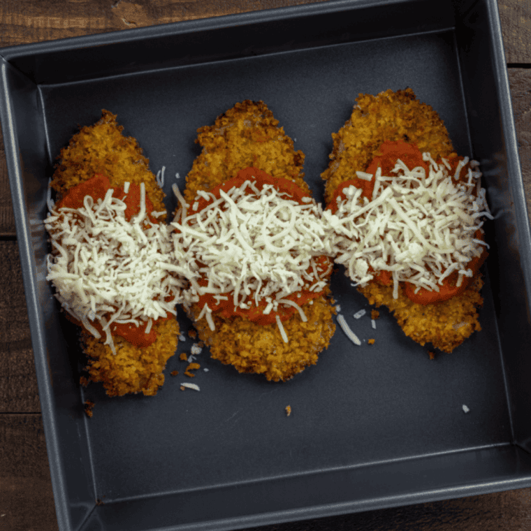 Breaded veal cutlets placed in the air fryer basket and sprayed with oil, ready to be cooked until golden brown.