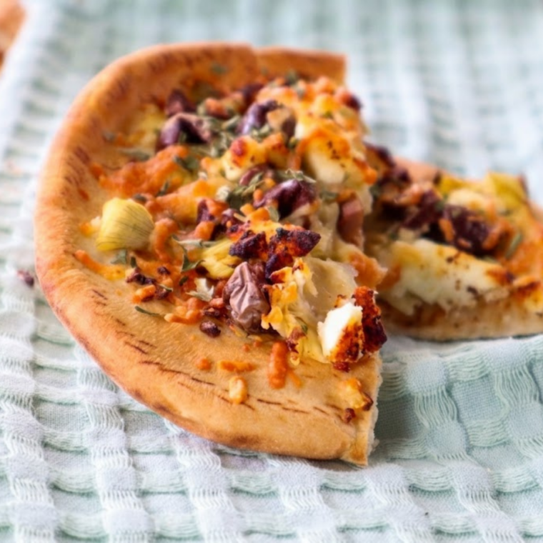 Air fryer artichoke and olive flatbread topped with artichoke hearts, olives, and melted cheese, sliced on a board