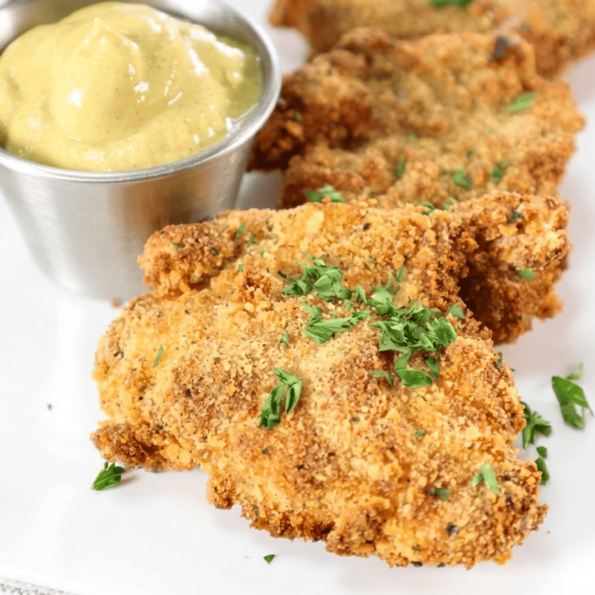 Crispy golden air fryer chicken thigh schnitzel served on a white plate with a lemon wedge
