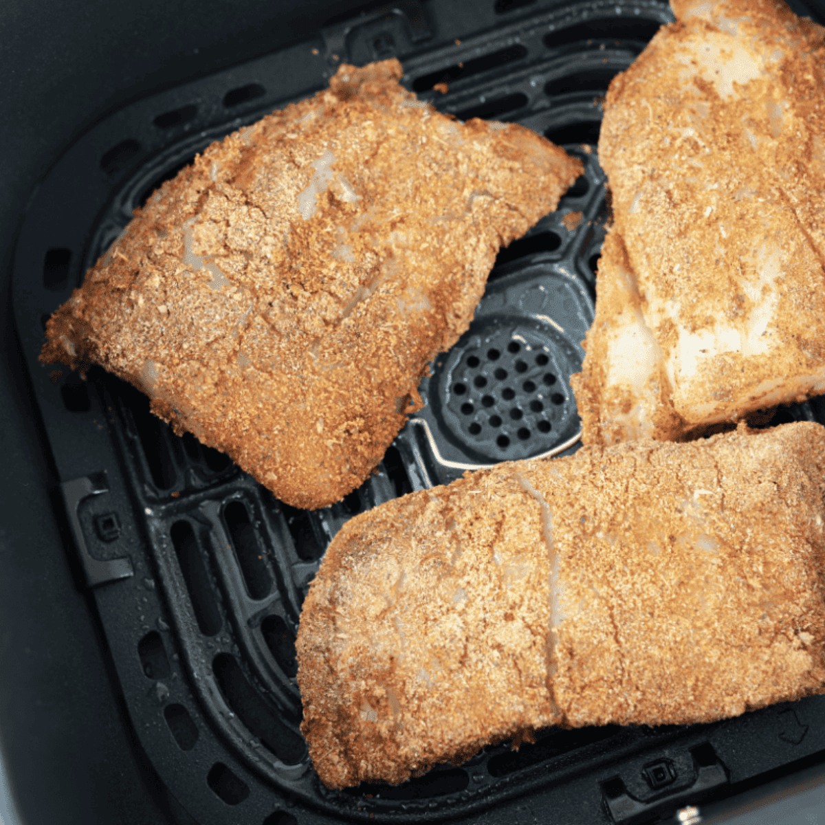 Seasoned red snapper fillets in air fryer basket, ready to cook, sprayed with oil