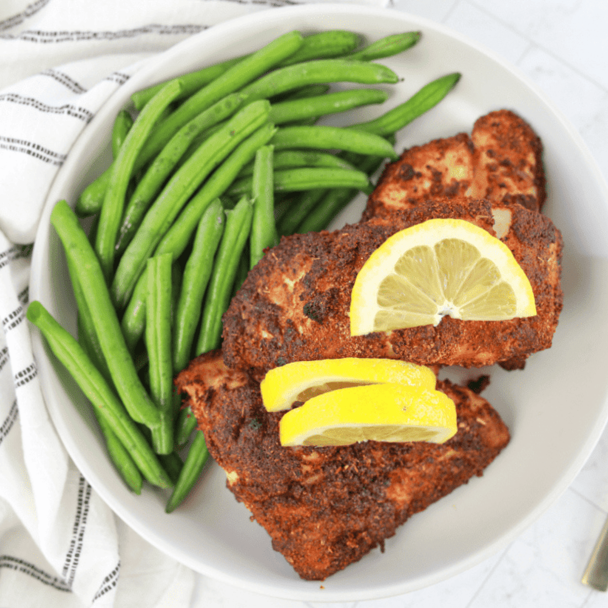 Air fryer cooked red snapper fillet, golden and flaky, served on a plate with lemon wedges and herbs