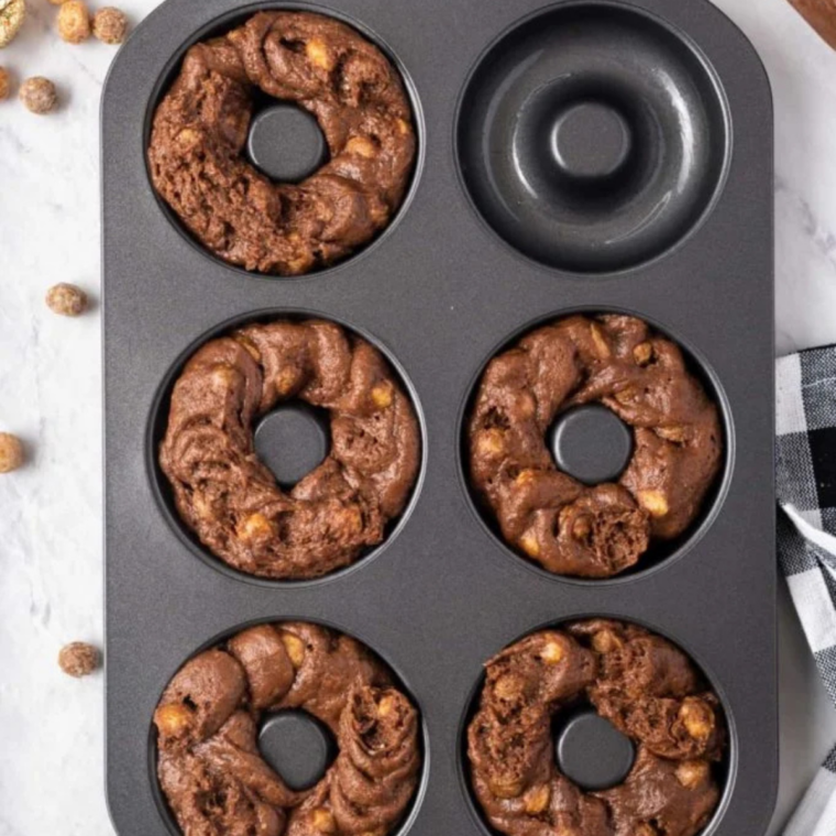 Chocolate donut batter piped into a six-cavity donut pan, each filled three-quarters full