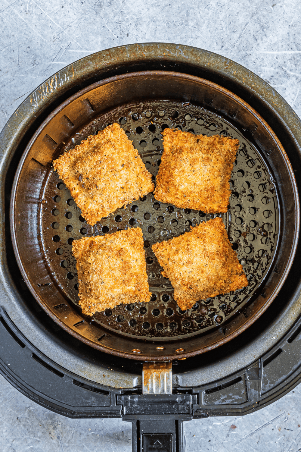 Frozen breaded ravioli arranged in the air fryer basket, cooking at 390°F, flipped halfway for even crispiness