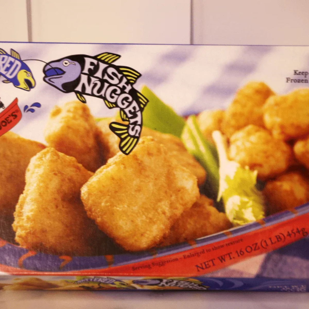 Box of frozen Trader Joe's battered fish nuggets with tartar sauce and an air fryer basket