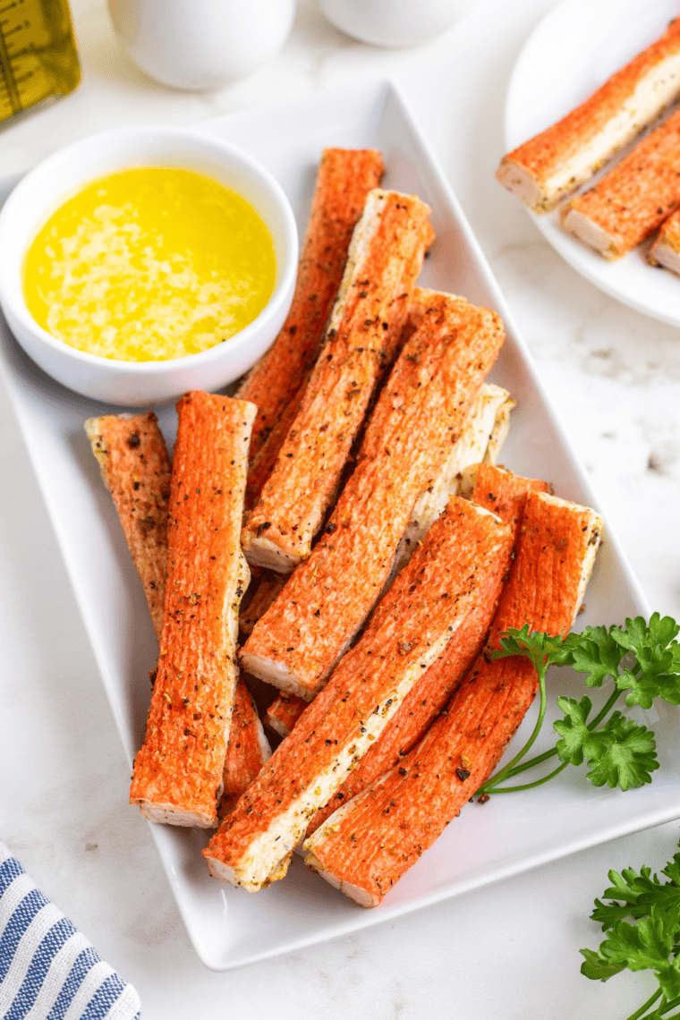 Crispy air fryer crab bites made with imitation crab and served with a buttery garlic dipping sauce on a white plate.