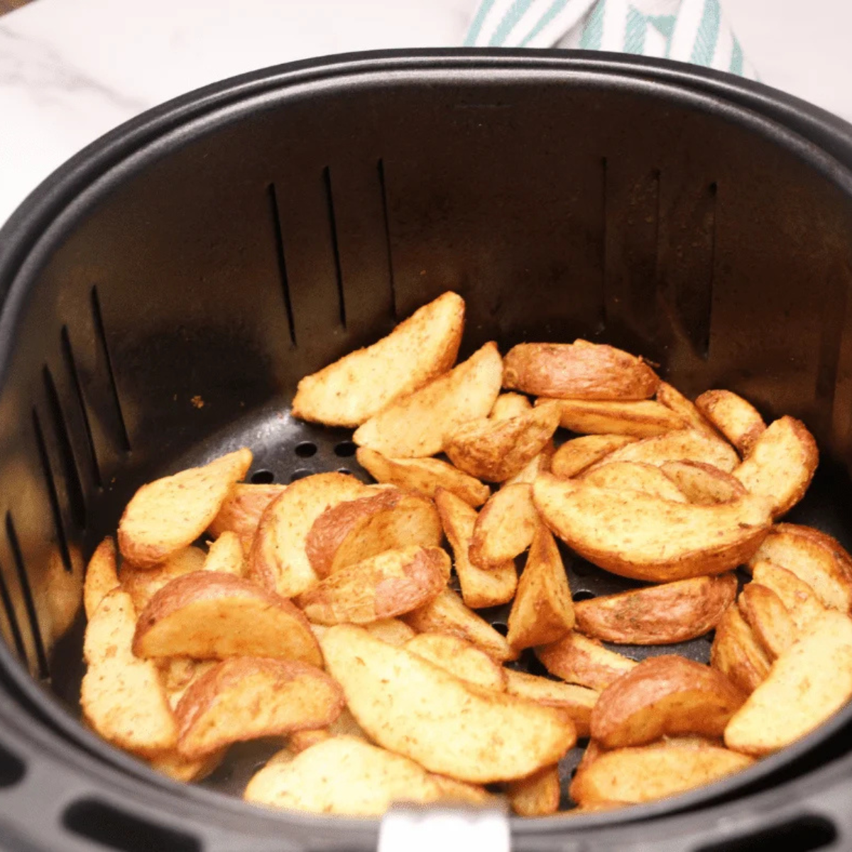 Air fryer frozen potato wedges partway through cooking and turning golden at the edges