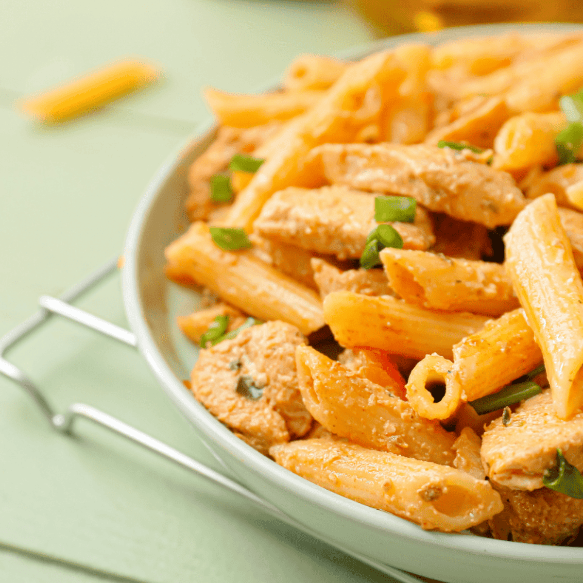 A bowl of creamy Cajun pasta topped with sliced air-fried chicken breast, sprinkled with red pepper flakes and fresh parsley.