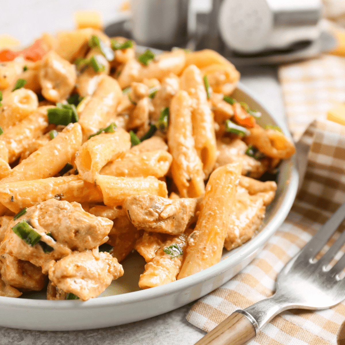 Close-up of a fork lifting creamy pasta noodles and a piece of spicy air fryer Cajun chicken.