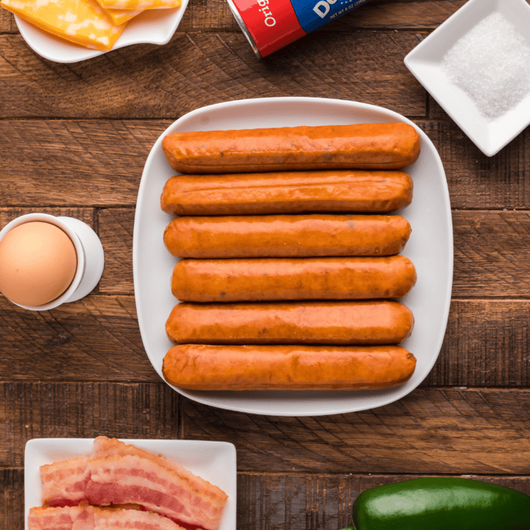 Hot dogs, pre-cooked bacon, cheddar cheese sticks, jalapenos, Pillsbury crescent rolls, egg, and sea salt laid out for air fryer pretzel cheese dogs