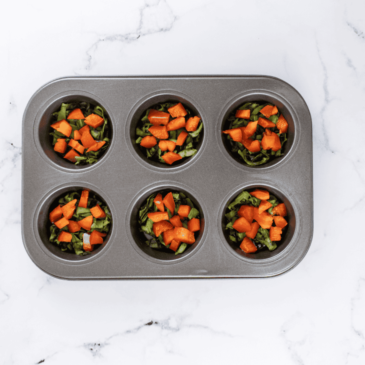 Filling muffin cups two-thirds full with spinach, red and green bell peppers, and tomatoes