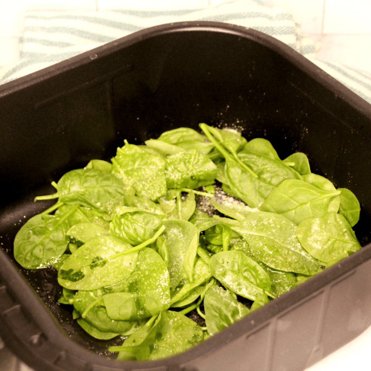Spinach leaves sprinkled with sea salt and seasoning before air frying.