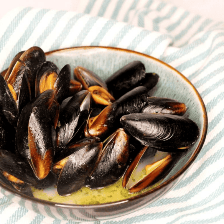 Mussels in air fryer basket drizzled with fresh lemon juice and sprinkled with chopped parsley, ready to serve.