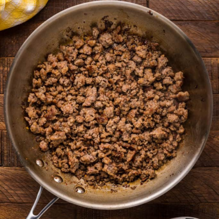 Ground beef browning and crumbling in a stainless skillet