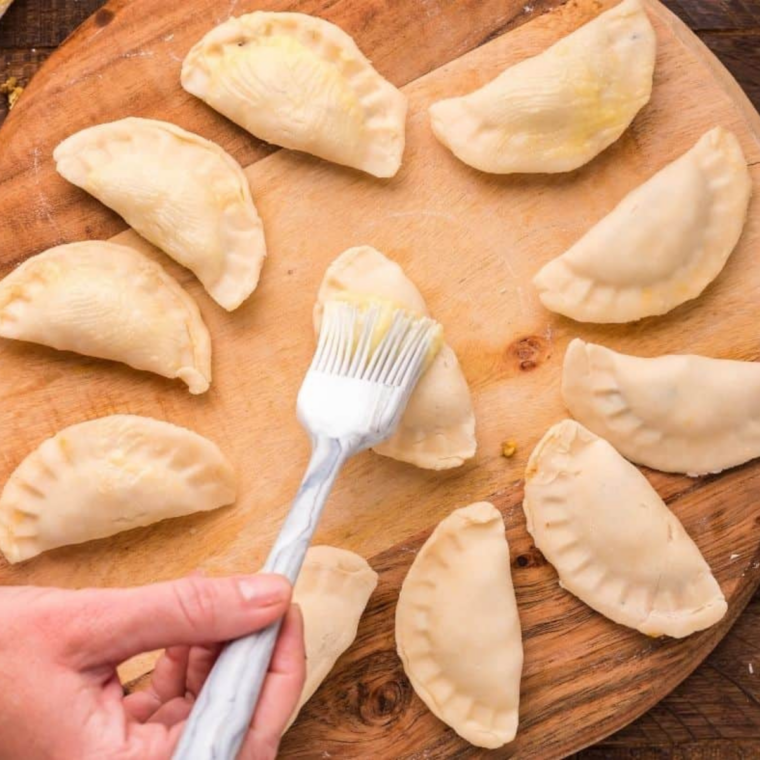 Uncooked beef empanadas brushed with melted butter in an air fryer basket in a single layer