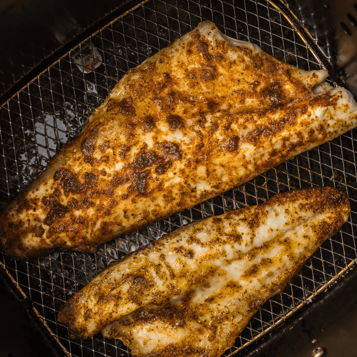 Golden, crispy air fryer branzino fillets served on a plate with lemon wedges.