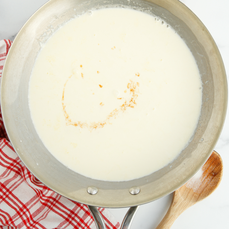 Heavy cream, vanilla, and salt simmering in a saucepan with a wire whisk