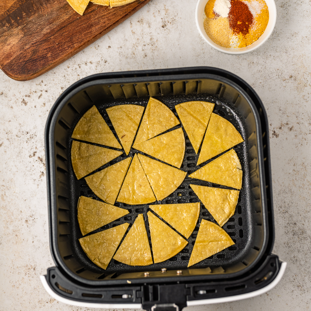 Tortilla wedges in a single layer in the air fryer basket, sprayed with oil and sprinkled with taco seasoning