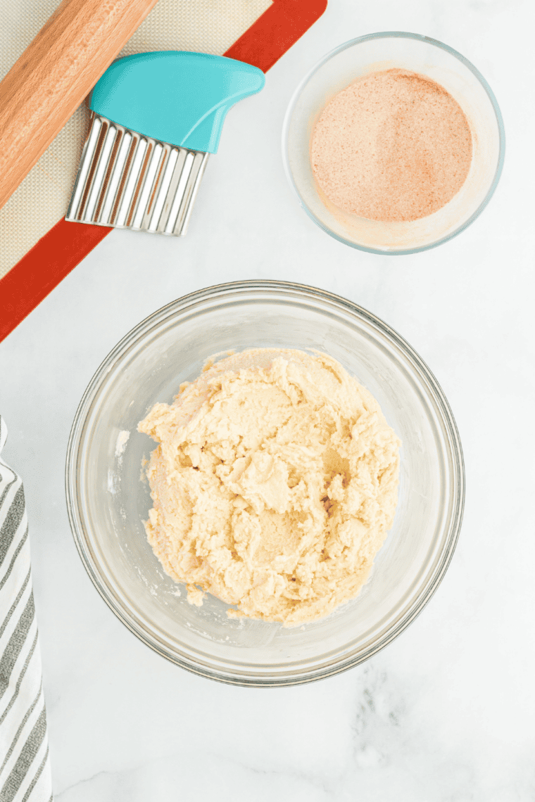 Mixing egg and vanilla into snickerdoodle dough, folding in dry ingredients gently, chilling dough, and preparing cinnamon sugar topping in a separate bowl.