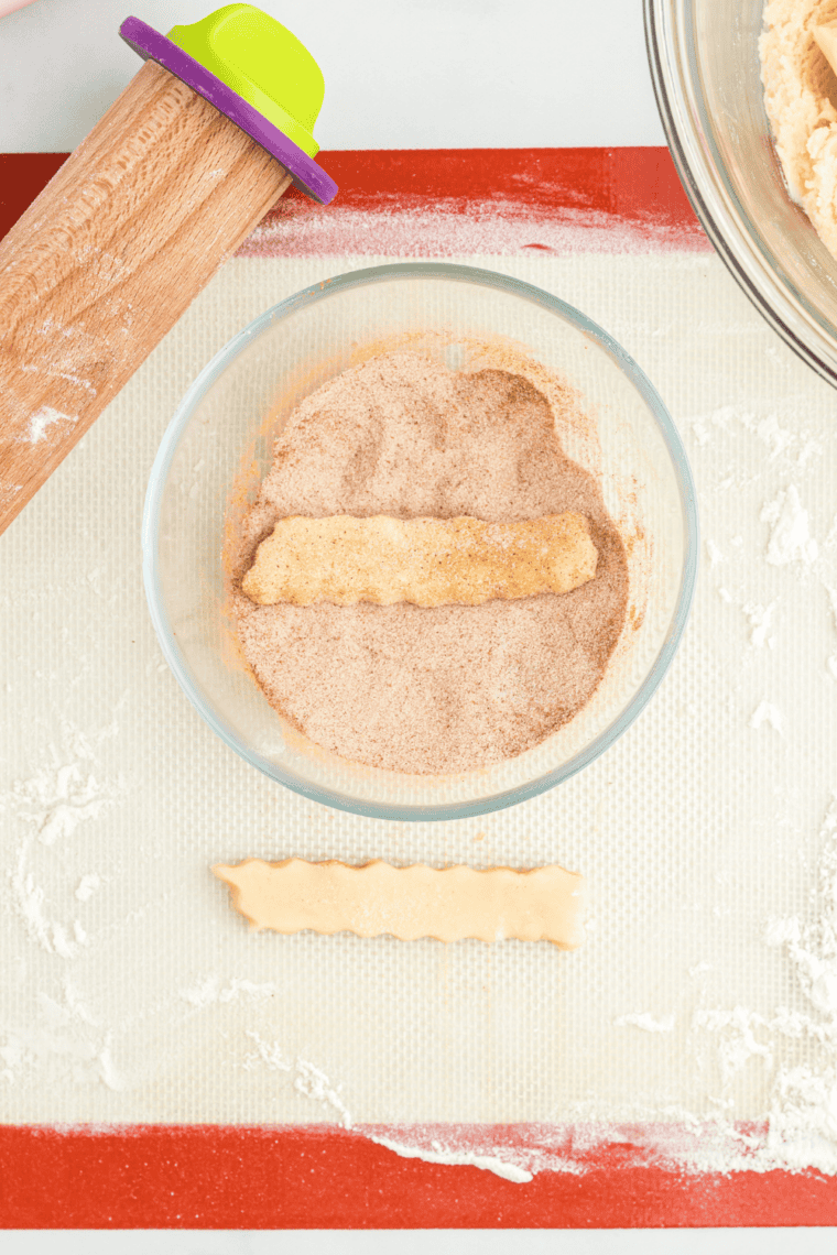 Rolling out a portion of snickerdoodle dough and cutting cookie fries ½”–¾” wide and 4”–5” long with a crinkle cutter.