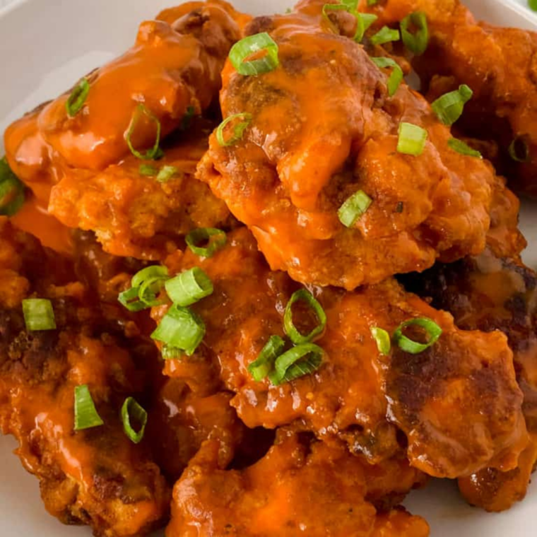 Golden-brown air fryer chicken tenders coated in buffalo sauce, served on a plate with celery sticks and a side of dipping sauce.