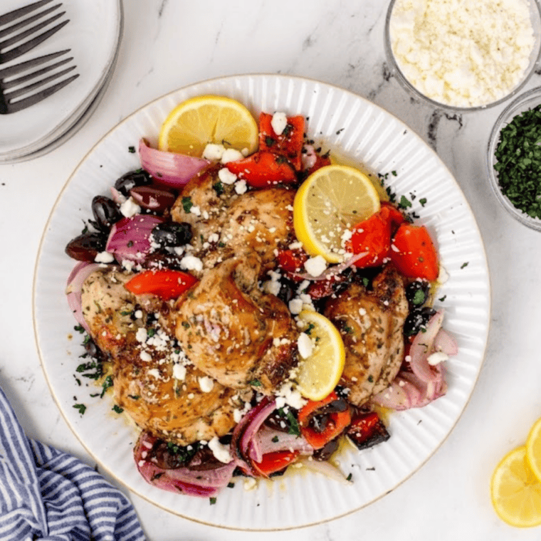 Air Fryer Greek Chicken with summer vegetables plated and topped with crumbled feta, chopped parsley, and lemon slices