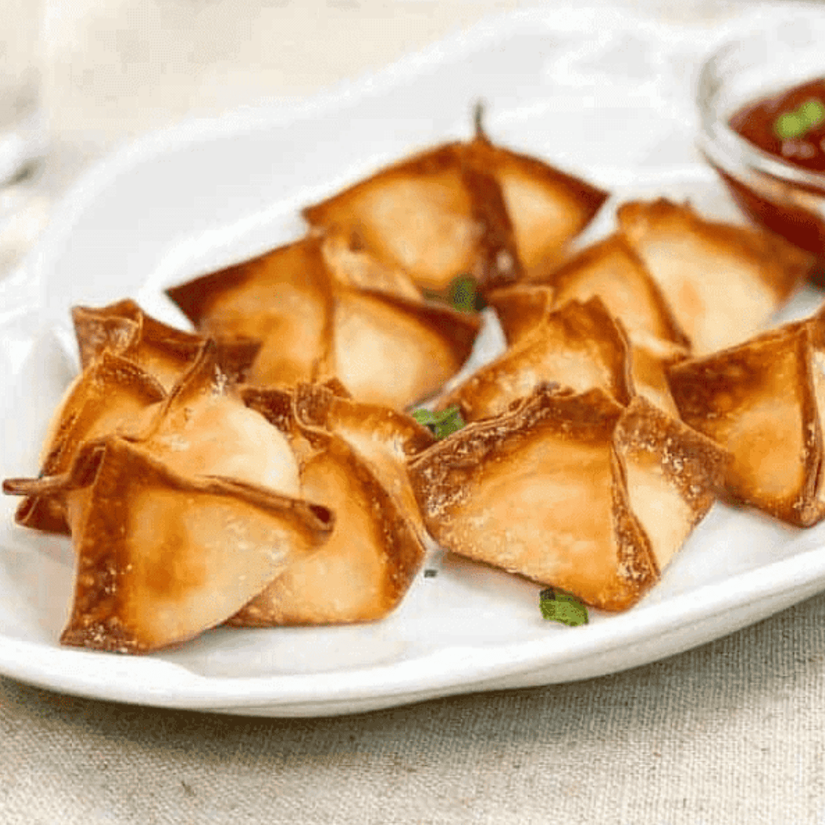 Golden crispy crab rangoon being reheated in an air fryer basket, showing crunchy edges and melted creamy filling inside.
