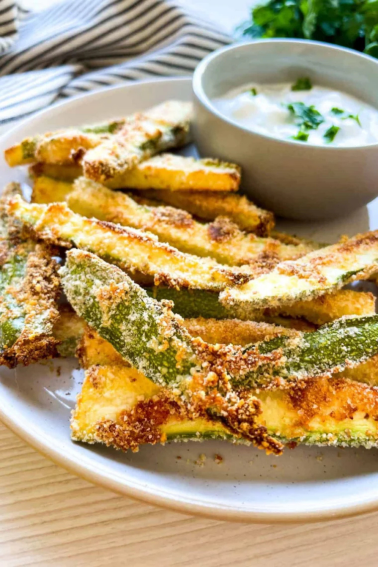 Hand dipping a crispy keto zucchini fry into garlic aioli