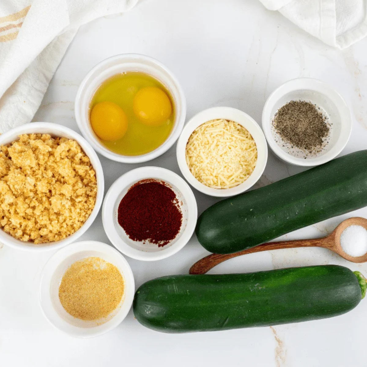 Ingredients for keto zucchini fries including zucchini, almond flour, grated parmesan, eggs, and seasonings