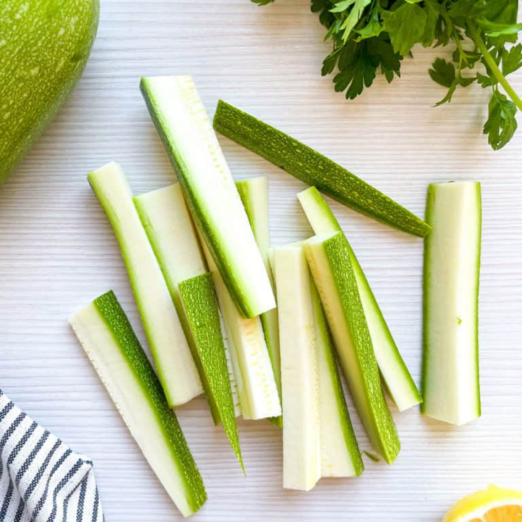 Zucchini sliced into thick fry-shaped sticks on a wooden cutting board