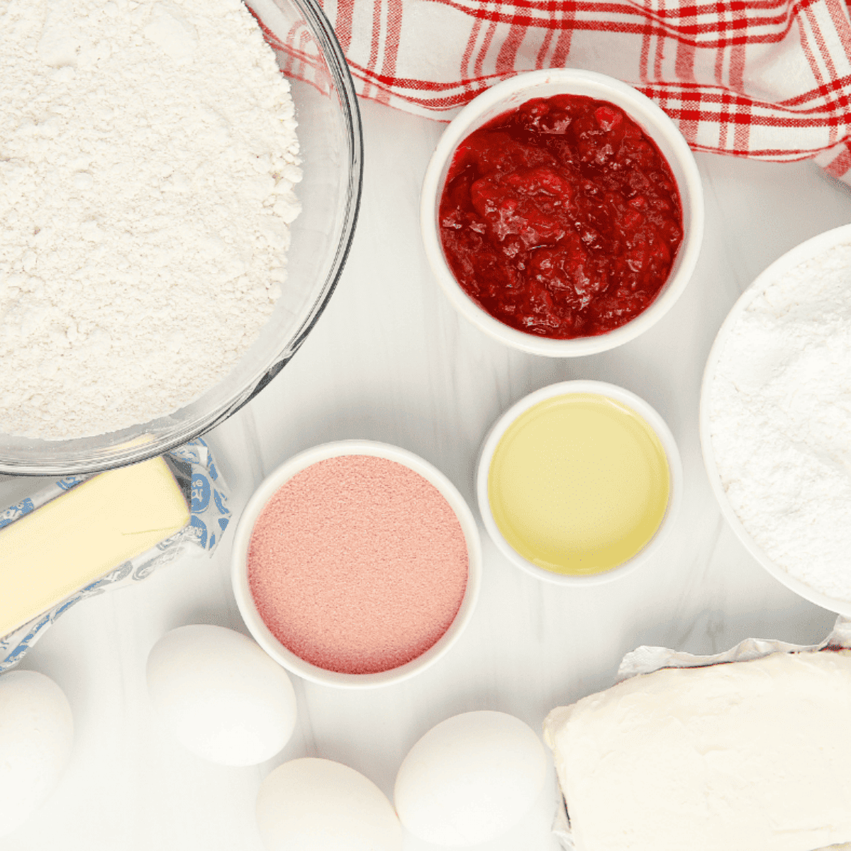 Cake mix, strawberry gelatin, eggs, jam, oil, and cream cheese laid out for air fryer strawberry cupcakes.
