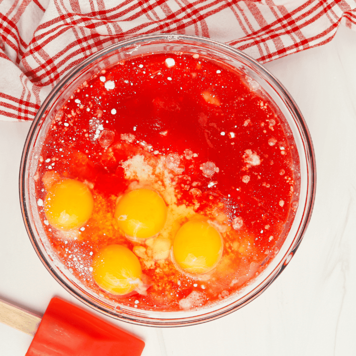 Pink strawberry cupcake batter being mixed in a large glass bowl.